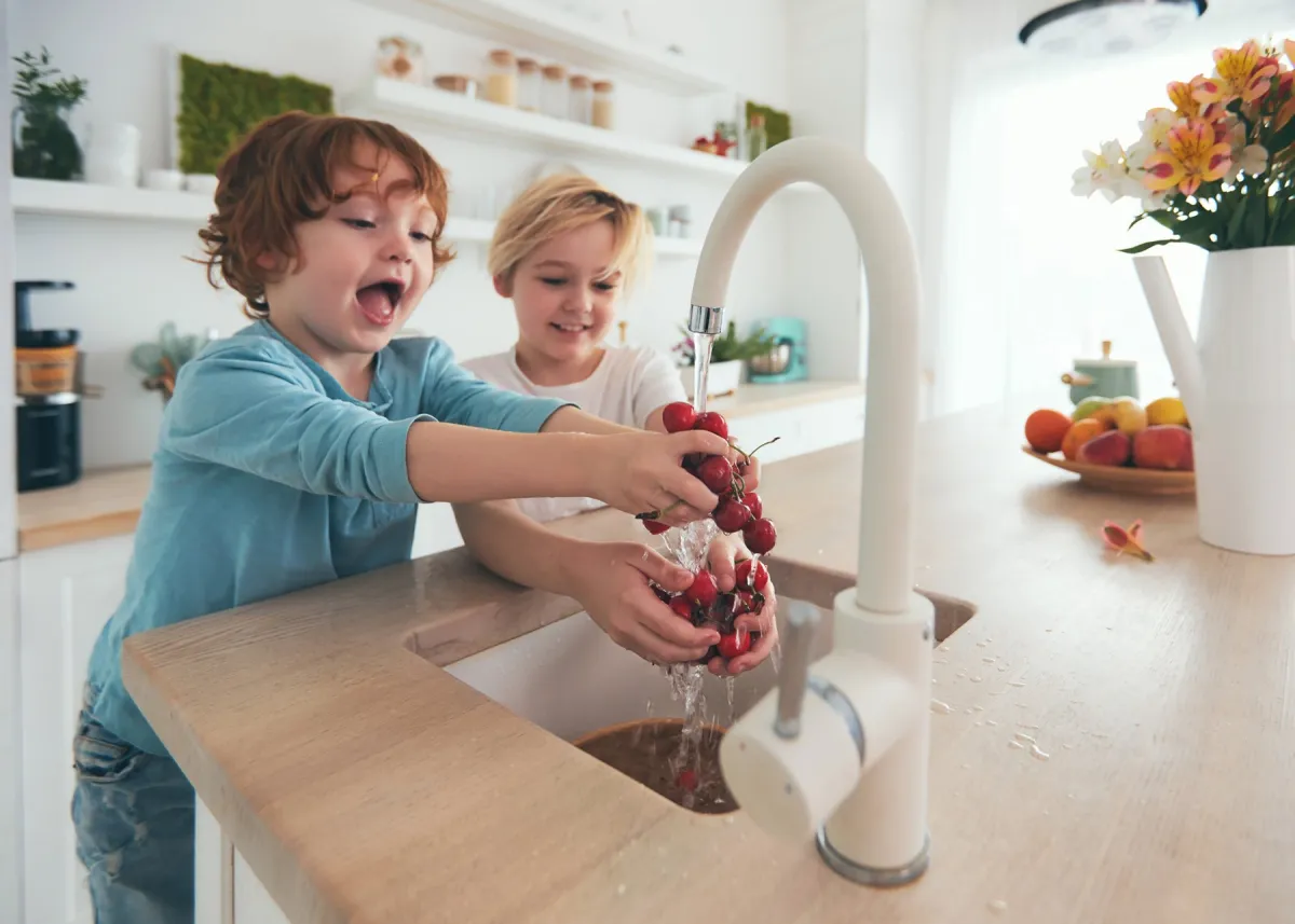 Two children rinsing fruit under the kitchen tap